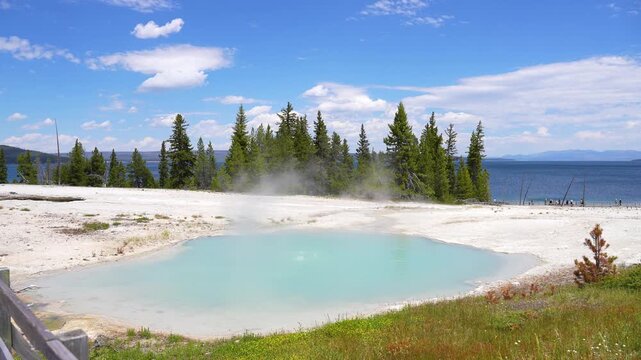 Close-up shot of vivid blue geothermal water formed by a geyser with Yellowstone Lake visible in the background at Yellowstone National Park, Wyoming.