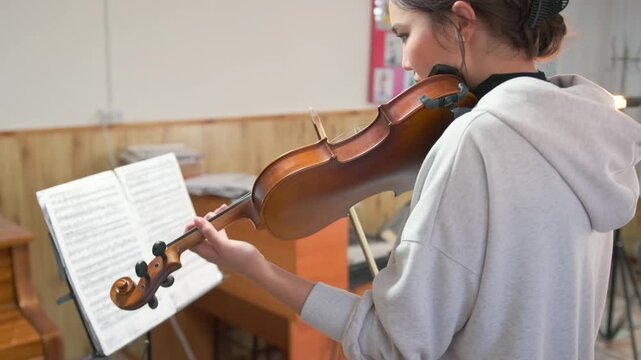 Close-up of a young female violinist playing during a music audition -  carefully following sheet music -  performing at audition with sheet music. Stage presence and musical literacy under pressure.