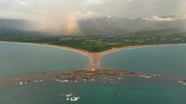 Drone footage of the Whale Tail sandbar in Uvita featuring dramatic clouds and a tropical rainbow over the Pacific coastline.