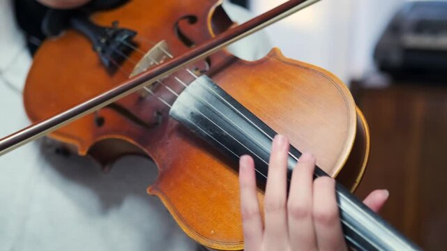 Violin being played by a young Asian musician. Bowing technique -  and the elegant detail of the wooden instrument. Artistic close-up for themes of classical music -  and dedication. -  craftsmanship