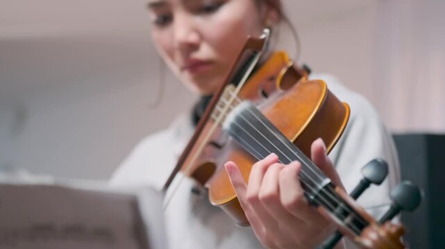 Close-up of young female violin student intensely preparing for upcoming classical music exam -  reads sheet music while practicing -  showing focus -  musical discipline. Student violinist preparing