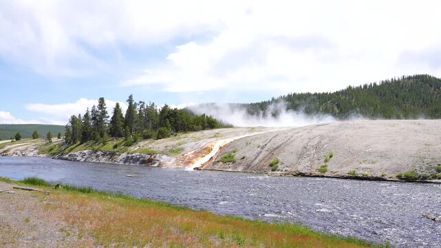 Shot of a geyser flowing and mixing with a river at Yellowstone National Park, Wyoming. Stunning geothermal scenery capturing the interaction of hot springs with flowing water in a dramatic natural la