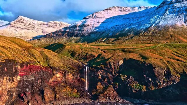 Dramatic waterfall cascadig over red volcanic cliffswith snow patches aerial vew