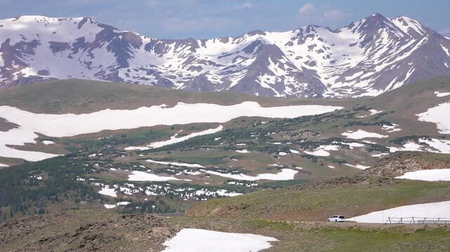 A car driving along Trail Ridge Road with massive snow-covered mountains in the background at Rocky Mountain National Park, Colorado