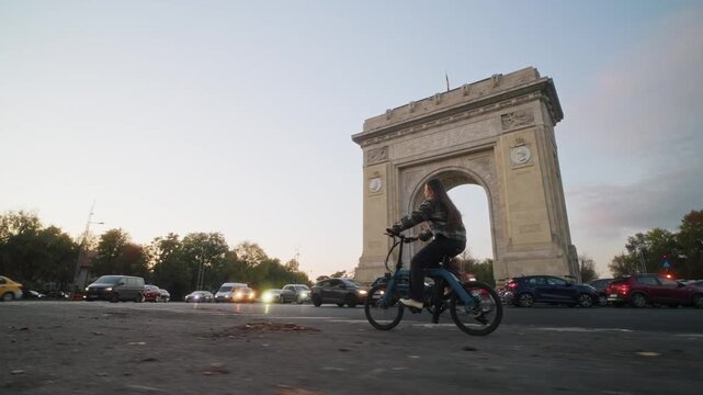 Urban cyclist passing arcul de triumf in bucharest during sunset