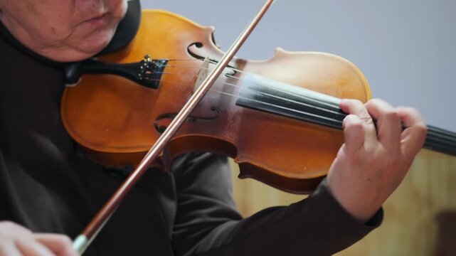 Mature Asian female musician passionately plays violin -  close-up view. Woman focused expression -  confident bowing convey deep emotion -  experience. Senior violinist performs expressive classical