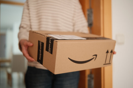 Alicante, Spain - February 02, 2026: Receiving Amazon online Order at home. Amazon prime delivery. Woman holding cardboard box with Amazon prime logo at home entrance