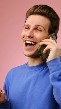 A happy young man talking on his smartphone and smiling during the conversation. Isolated on a pink background. Vertical video.