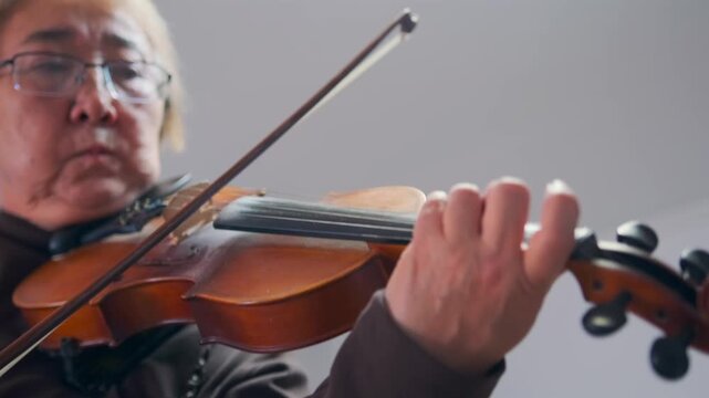 Close-up of inspiring Asian music teacher performing classical violin. Expressive bowing -  emotional presence during lesson or practice session. Asian violin teacher playing with passion and