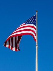 Obraz premium American Flag Flown On Pole Against Clear Blue Sky, Symbol of Freedom and Patriotism Outdoors