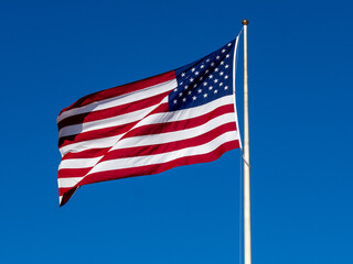 Obraz premium American Flag Waves Proudly in Clear Blue Sky Over a Tall Flagpole