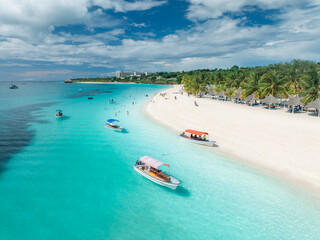 Obraz premium Beautiful tropical beach with turquoise sea and white sand in Kendwa, Zanzibar. Aerial view of coastline with palm trees, clear water, boats, resort. Summer vacation, travel, exotic. Top drone view