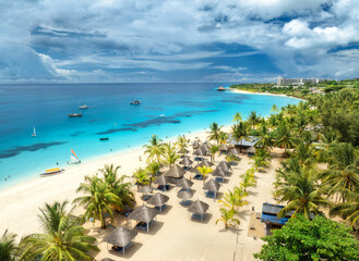 Obraz premium Aerial view of white sandy beach with palm trees, umbrellas, yachts, boats, blue sea, sky with clouds at summer day. Vacation in Kendwa, Zanzibar island. Tropical landscape. Turquoise sea. Top view