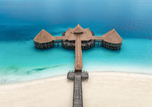 Aerial top down view of a wooden pier with thatched roof over turquoise water in Zanzibar. Sea, bungalow, jetty on white sand beach in Nungwi, Tanzania. Luxury resort background for travel destination
