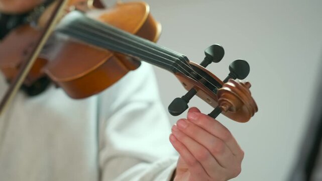 Close-up of a young musician adjusting violin tuning pegs by hand. The fingers carefully turn the pegs while holding the instrument -  showing the fine process of tuning. Instrument maintenance.