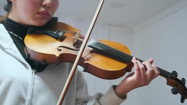 Close-up of a violin in the hands of a young musician. Focus on the wooden texture -  and bow movement during a music lesson or home practice. Calm indoor setting with natural light. -  strings