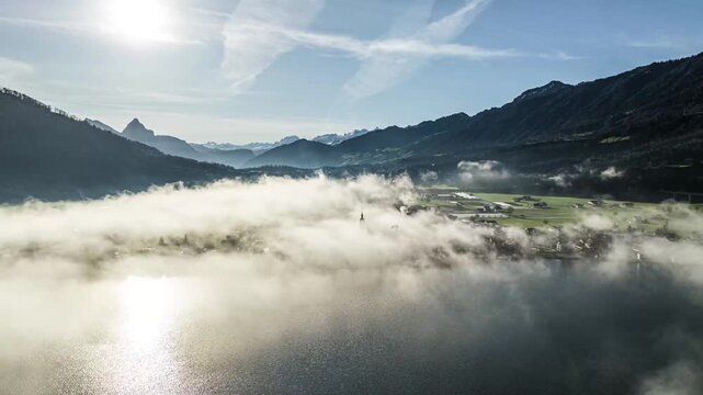 Backlit aerial shot of fogy alpine valley with sun fare and mountains