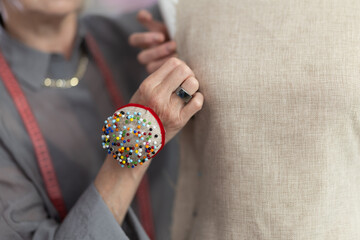 Hands of an experienced seamstress with a pin pad work with a fabric sample, making marks. Dressmaker pinning fabric with pins close-up © JackF