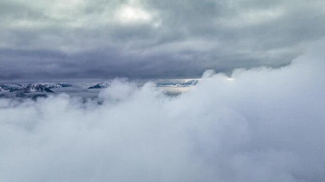 Moody aerial view of mountain peaks rising from dark ea of clouds