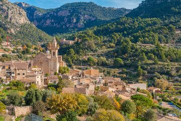Obraz premium Valldemossa on a sunny day in Mallorca, featuring charming stone houses, narrow historic streets, lush greenery, and mountain scenery. A picturesque village known for its Mediterranean charm 