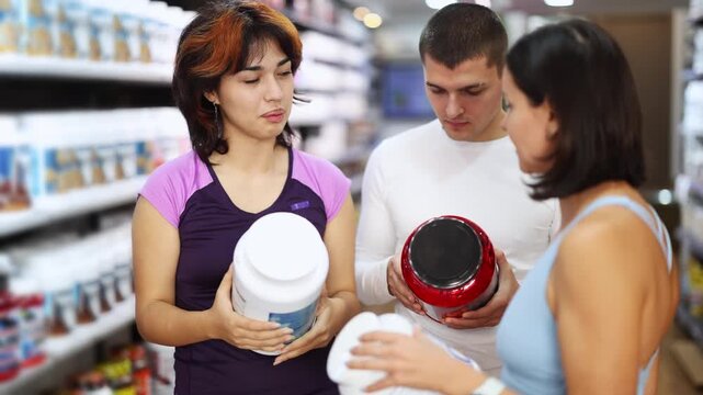 Undetermined male and female customers reviewing jars of protein in sports food shop