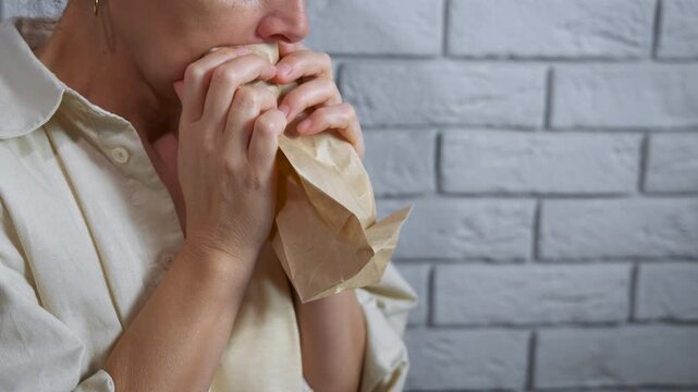 Stressed woman breathing into paper bag for panic attack. Distressed woman suffering from anxiety and hyperventilating, breathing into a paper bag to calm down her panic attack