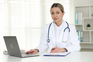 Portrait of cardiologist with laptop, pen and clipboard at table in clinic