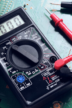 High angle view digital multimeter with connected red and black test leads on green electronic circuit background.