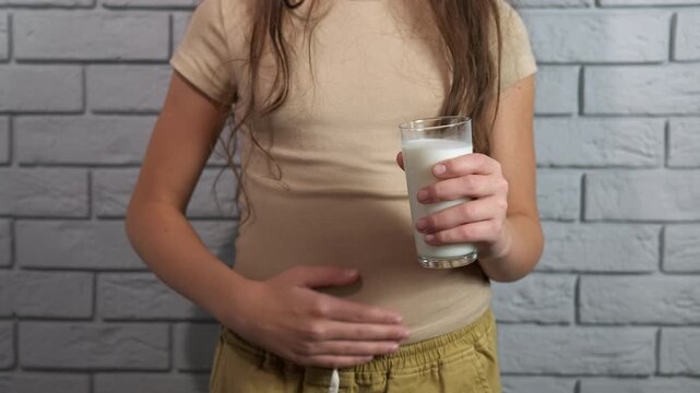 Girl experiencing stomach pain from lactose intolerance. Young girl holding a glass of milk and rubbing her stomach, experiencing abdominal pain and discomfort from lactose intolerance