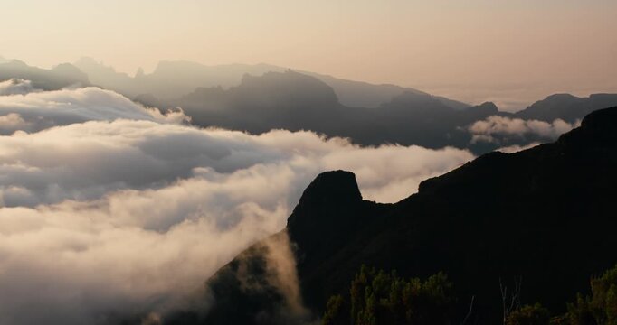 Cloud motion as flowing water over mountainous terrain at dawn. Low clouds cover valleys and reveal ridgelines during sunrise. Madeira island, Bica da Cana viewpoint