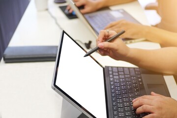Person's hand uses a stylus on a modern laptop screen with a bright white mockup, demonstrating digital work and creativity. The clean desk setup, conveys focused productivity.