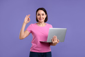 Woman with laptop showing ok gesture on purple background