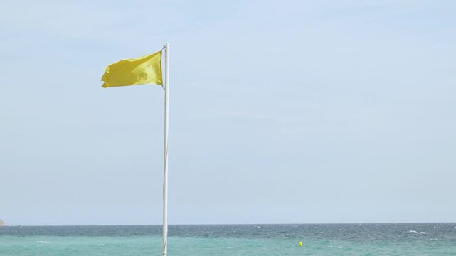 Yellow beach flag warning of caution on calm ocean