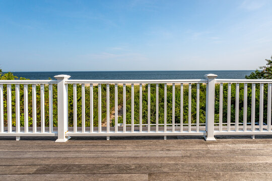 Ocean view from wooden deck with white railing overlooking coastal dunes and blue sea under clear sky
