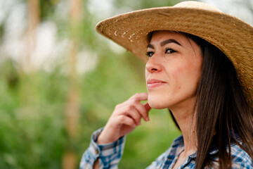 Portrait of a young female farmer wearing a straw hat in a greenhouse