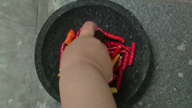 the activity of grinding cayenne pepper, curly chilies, and garlic manually using a mortar and pestle