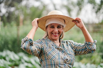 Smiling female farmer wearing a straw hat and plaid shirt standing in a vegetable garden.