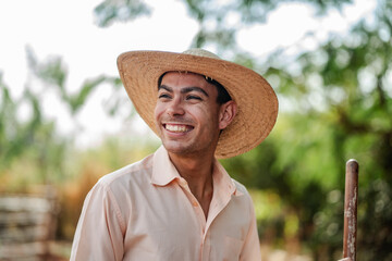 Portrait of a happy young male farmer wearing a straw hat and smiling while working outdoors in a...