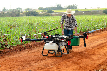 Obraz premium Farmer preparing a large industrial agricultural drone for crop spraying on a dirt road next to a green field
