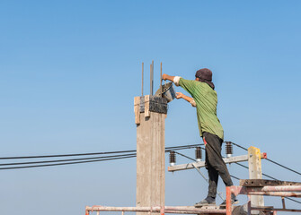 Construction worker standing on scaffolding pouring wet concrete from a bucket into a pillar formwork.