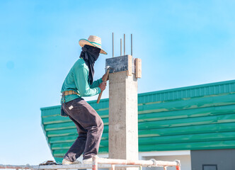 Construction worker on scaffolding using a hammer to secure wooden formwork on a concrete pillar.