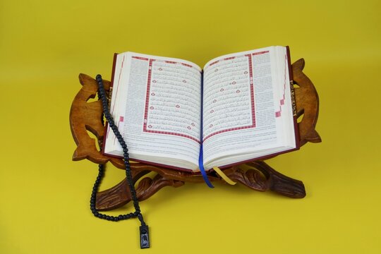 Open Quran on Wooden Prayer Stand with Colorful Tasbih and Bookmark. Ramadan and Islamic concept. isolated on yellow background