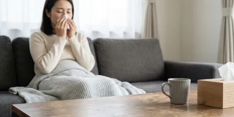 Home woman winter disease health with korean season unhealthy ache allergy asia autumn blanket blowing on sofa under warm throw tissue box and hot drink on wooden table