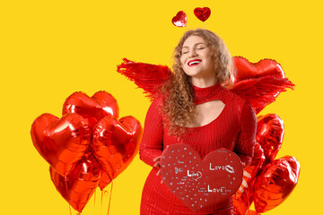 Fototapeta premium Beautiful woman dressed as Cupid with card and balloons on yellow background. Valentine's Day celebration
