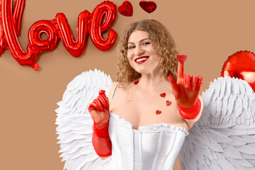 Fototapeta premium Sexy young woman dressed as Cupid with heart and balloons on beige background. Valentine's Day celebration