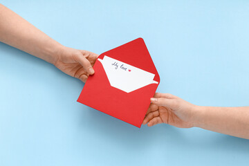 Obraz premium Female hands with envelope and love letter on blue background. Valentine's Day celebration