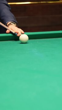 Vertical close-up of pool player tapping cue ball, popping it off green felt for a jump trick during billiards&mdash;shallow focus, cinematic b-roll with copy space.