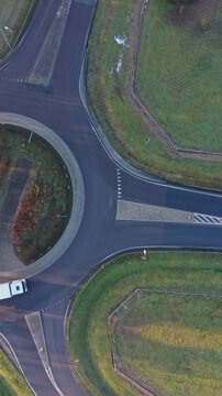 Vertical Screen Aerial View Circular Intersection With Moving Vehicles. Coach And Cars Navigating Painted Lanes Around Landscaped Island, Smooth Traffic Flow, Morning Shadows, Clear Asphalt