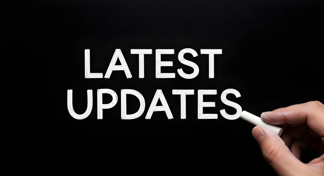 Hand writing the words latest updates on a black chalkboard with white chalk for important notifications