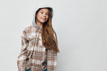 Naklejka premium Teenage girl with long hair wearing a hooded sweatshirt and plaid shirt, smiling and posing against a light background for casual style and youth fashion portrait.